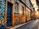 Façade colorée recouverte d'azulejos le long d'une rue pentue de Porto, carreaux bleus et ocres, textures usées, pavés au premier plan, lumière douce du coucher de soleil, ambiance réaliste et naturelle.