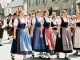 Des jeunes femmes en costumes traditionnels bretons participent à une cérémonie estivale à Quimper, avec un bagad en arrière-plan.