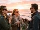 Trois observateurs, deux femmes et un homme, portent des lunettes d’éclipse sur une côte bretonne au coucher du soleil, près d’une petite enceinte portable.