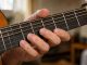 Gros plan sur la main gauche d’un homme formant proprement un accord de si mineur sur une guitare acoustique.