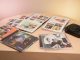 Table de collectionneur présentant quatre albums de musique physiques ouverts, des photocards colorées, des livrets photo et un lecteur CD sous une lumière douce de studio.